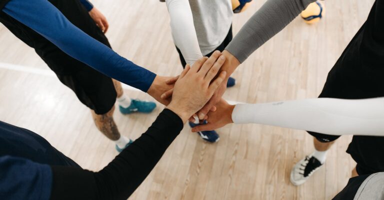 Close-up of athletes joining hands in a motivational sports huddle on an indoor court.
