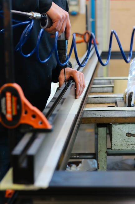 A worker carefully drills metal with precision in an industrial workspace, focusing on craftsmanship.